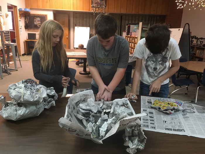 Three students use newspaper to make STEM snowmen. 